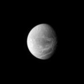 Bright lines creep across the face of Dione. The lines are systems of geologically fresh-looking canyons with bright, icy walls