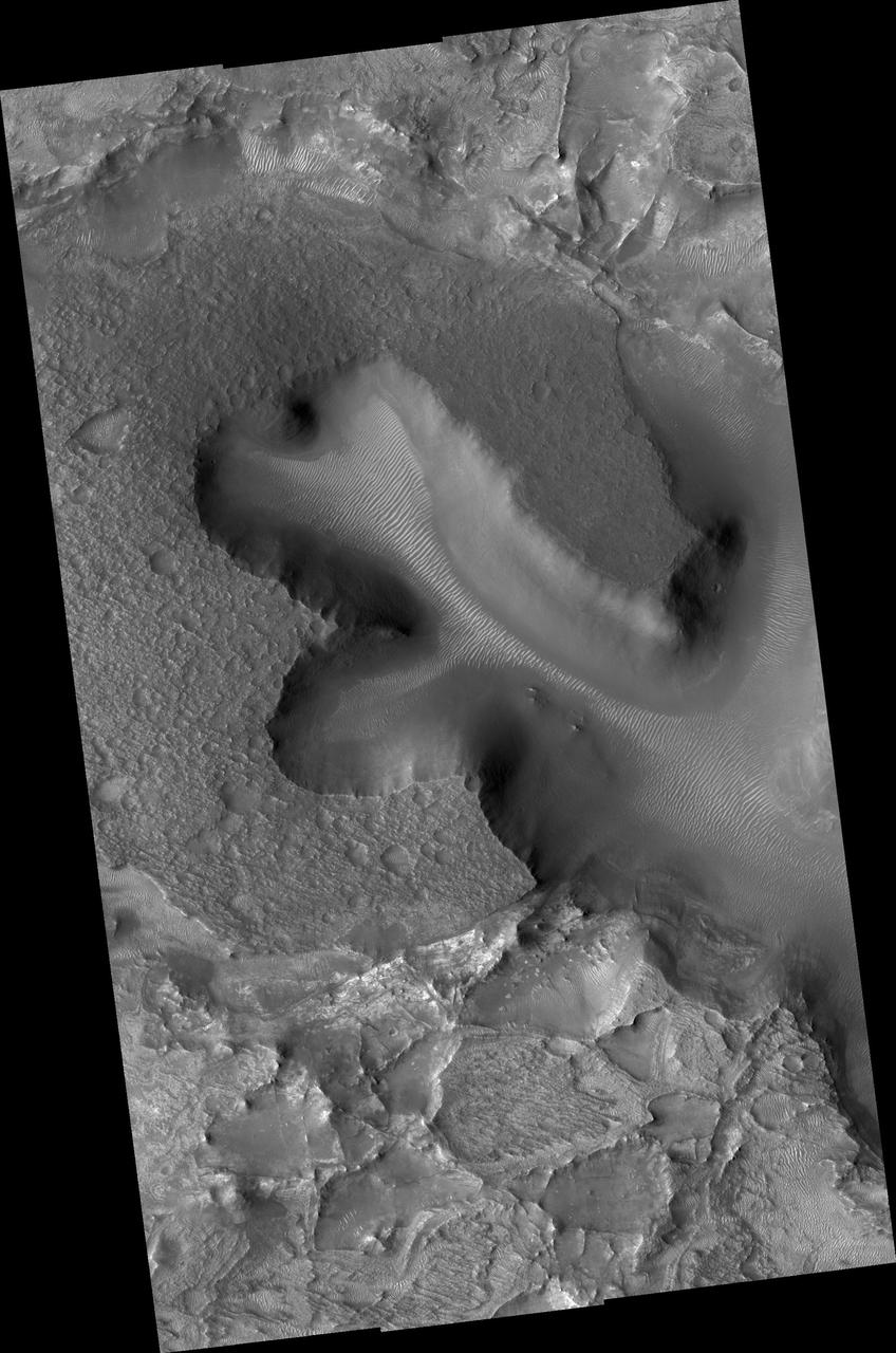 NASA Mars Reconnaissance Orbiter shows densely fractured light-toned rock in the vicinity of the Nili Fossae. The light-toned material is finely layered; these layers can be seen in cross-section along a scarp face at the bottom of the image.
