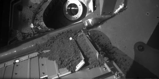This image shows a sample of Martian soil resting on a screen over the opening to one of the eight ovens of the Thermal and Evolved-Gas Analyzer instrument TEGA on NASA Phoenix Mars Lander. 