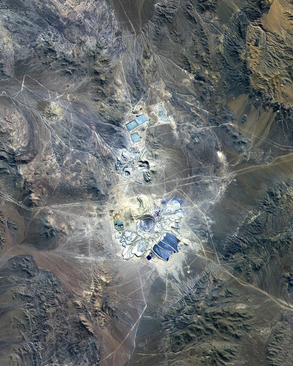 This ASTER image covers 30 by 37 km in the Atacama Desert, Chile and was acquired on April 23, 2000. The Escondida Cu-Au-Ag open-pit mine is at an elevation of 3050 m, and came on stream in 1990. Current capacity is 127,000 tons/day of ore; in 1999 production totaled 827,000 tons of copper, 150,000 ounces of gold and 3.53 million ounces of silver. Primary concentration of the ore is done on-site; the concentrate is then sent to the coast for further processing through a 170 km long, 9 pipe. Escondida is related geologically to three porphyry bodies intruded along the Chilean West Fissure Fault System. A high grade supergene cap overlies primary sulfide ore. This image is a conventional 3-2-1 RGB composite. Figure 1 displays SWIR bands 4-6-8 in RGB, and highlights lithologic and alteration differences of surface units. The image is located at 24.3 degrees south latitude and 69.1 degrees west longitude. http://photojournal.jpl.nasa.gov/catalog/PIA11090
