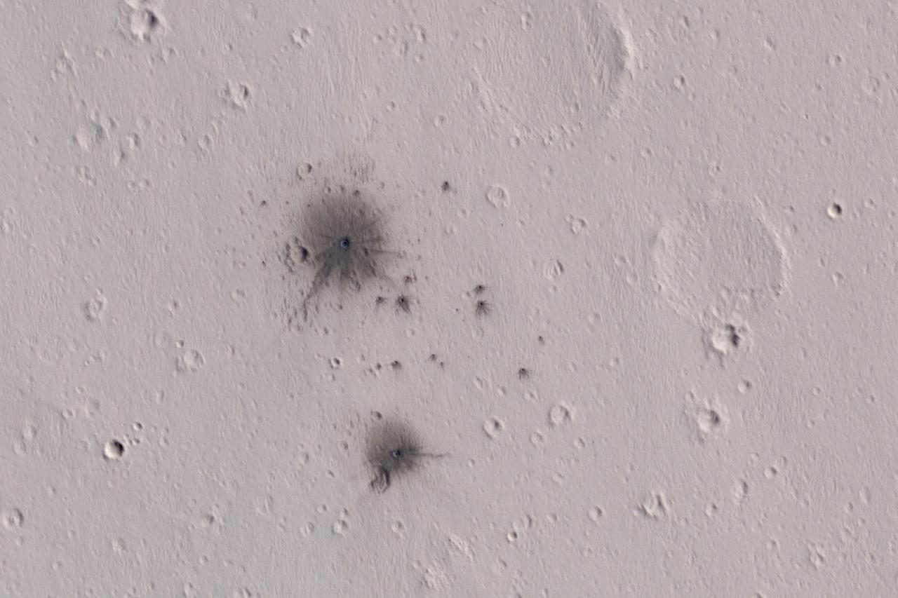 The dark spots in this enhanced-color infrared image are the recent impact craters that occurred in the Tharsis region between 2008 and 2014. These impact craters were first discovered by the Mars Context Camera (or CTX, also onboard the Mars Reconnaissance Orbiter) as a cluster of dark spots. The meteoroid that formed these craters must have broken up upon atmospheric entry and fragmented into two larger masses along with several smaller fragments, spawning at least twenty or so smaller impact craters. The dark halos around the resulting impact craters are a combination of the light-toned dust being cleared from the impact event and the deposition of the underlying dark toned materials as crater ejecta. The distribution and the pattern of the rayed ejecta suggests that the meteoroid most-likely struck from the south. http://photojournal.jpl.nasa.gov/catalog/PIA11176