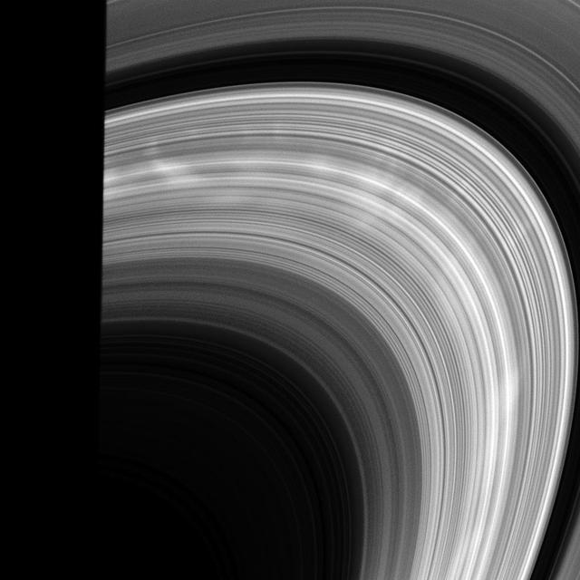 Bright spokes emerge from behind the shadow of the planet and into sunlight in this view from the Cassini spacecraft.