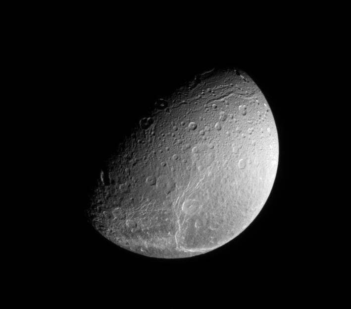 The Cassini spacecraft looks down on the north pole of Dione and the fine fractures that cross its trailing hemisphere.