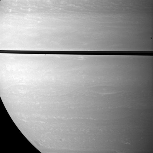 While studying Saturn atmosphere, NASA Cassini spacecraft happens to catch a view of two small, icy satellites. Mimas drifts past on the far right of the image. Janus appears as a black dot just below the rings near the center of the image.
