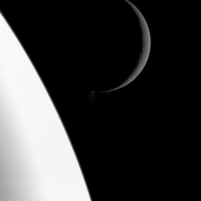 NASA Cassini spacecraft captures this scene showing the bright crescent of Saturn moon Enceladus at top right. The center of the image reveals plumes of water ice spew out from fractures known as tiger stripes near the south pole of the moon.
