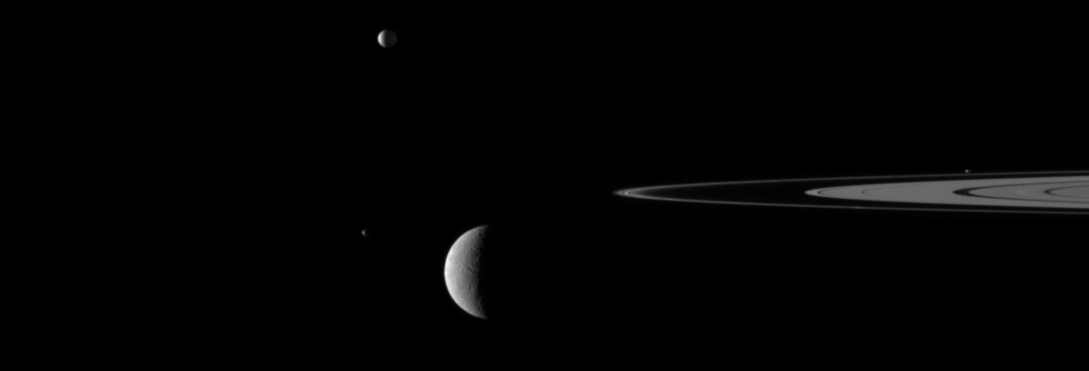 A gaggle of moons parade around Saturn rings in this image from NASA Cassini spacecraft in which the large moon Rhea passes in front of the small moon Janus. Go to the Photojournal to view the animation.