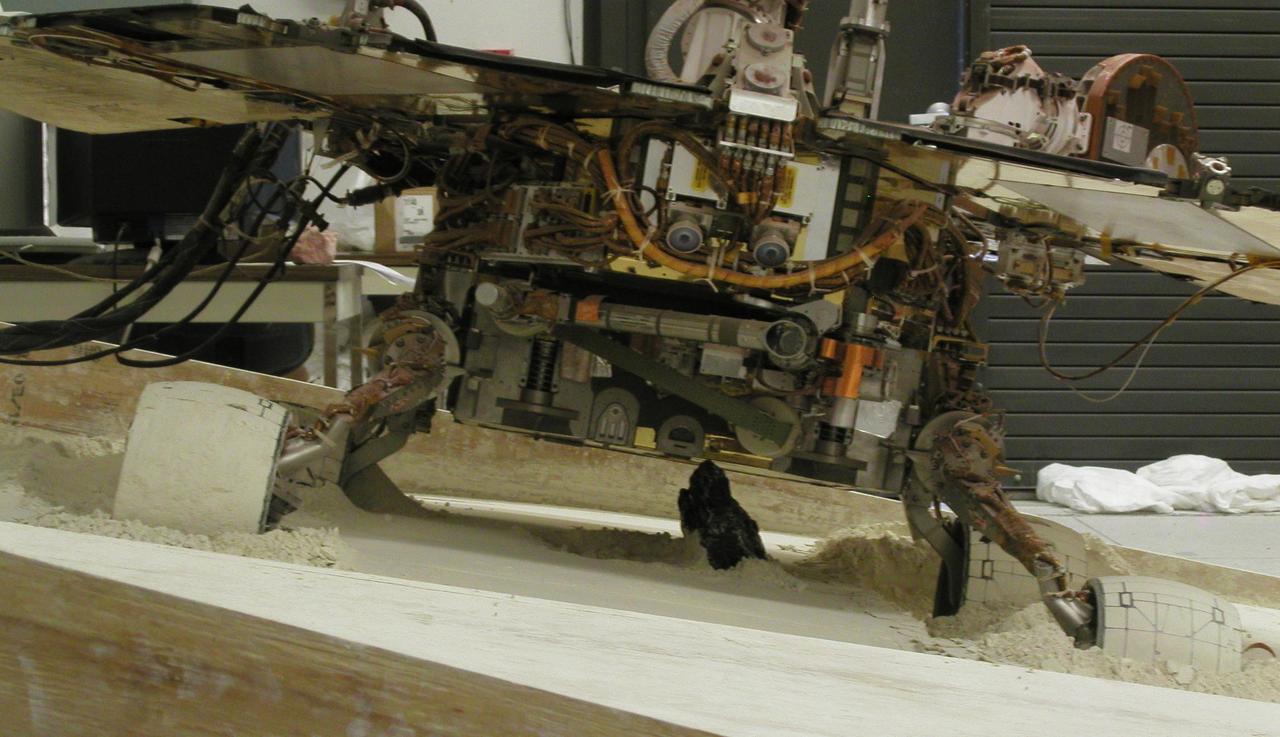 With a slope of about 10 degrees and a pointy rock under the test rover belly, this sandbox setup at NASA JPL, is ready for engineers to use the test rover to assess possible moves for getting Mars rover Spirit out of a patch of loose Martian soil.