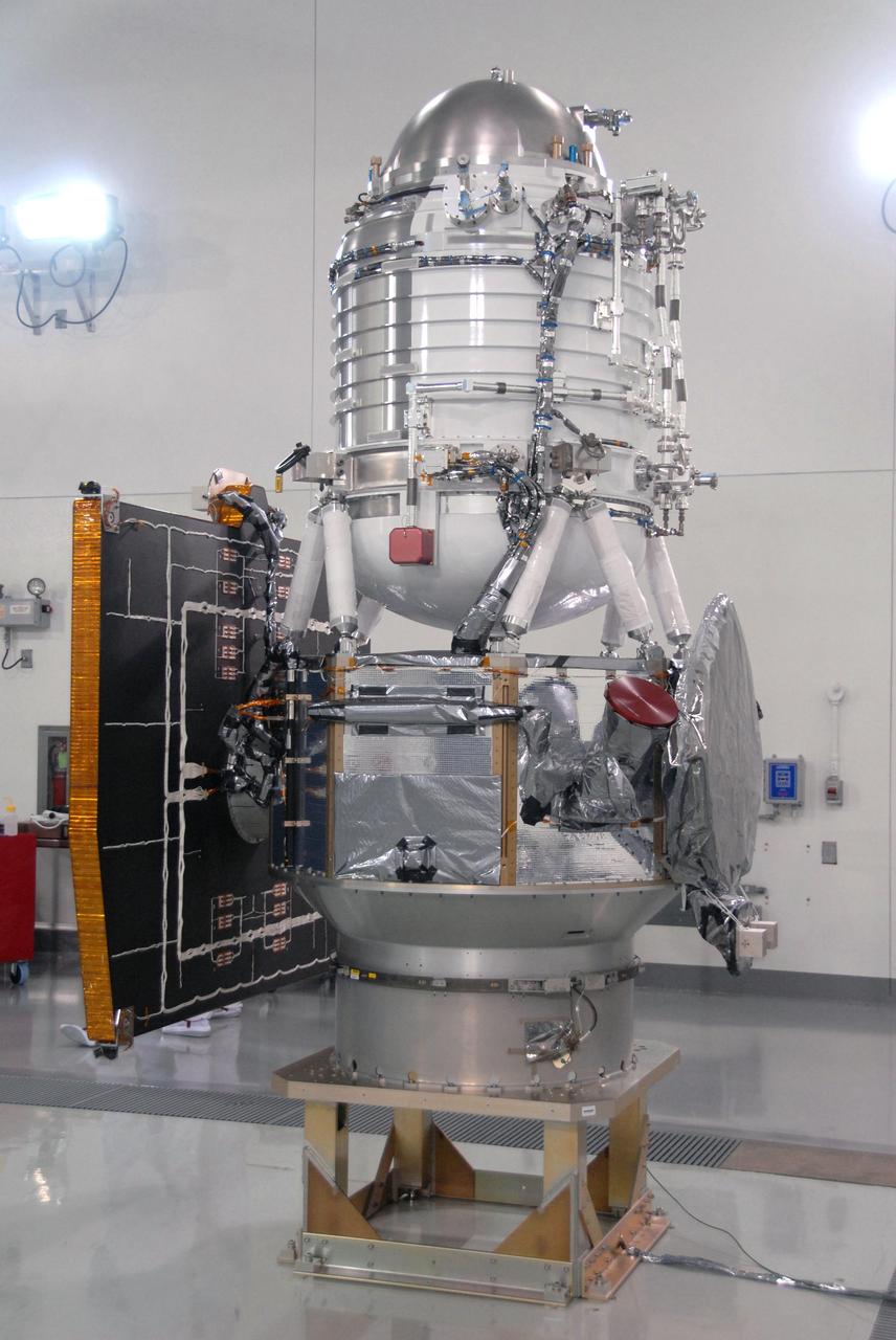 NASA Wide-field Infrared Survey Explorer spacecraft is situated on a work stand. At left on the spacecraft is the fixed panel solar array. In front, the square is the HGA Slotted Array Ku-Band. 