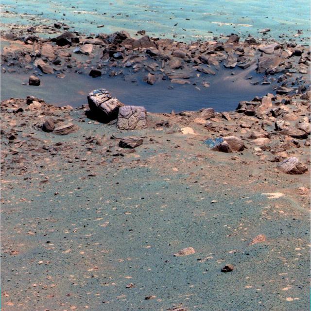 This false-color image, taken by the panoramic camera on NASA rover Opportunity, shows the rock Chocolate Hills, perched on the rim of the 10-meter 33-foot wide Concepcion crater. This rock has a thick, dark-colored coating resembling chocolate.