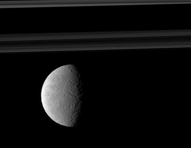 Rhea trailing hemisphere shows off its wispy terrain on the left of this image taken by NASA Cassini spacecraft which includes Saturn rings in the distance.