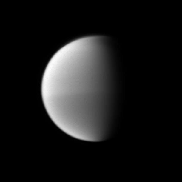 Titan seasonal hemispheric dichotomy is chronicled in black and white, with the moon northern half appearing slightly lighter than the dark southern half in this image taken by NASA Cassini spacecraft.