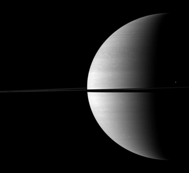 The moon Tethys stands out as a tiny crescent of light in front of the dark of Saturn night side. Tethys can be seen above the ringplane on the far right of this NASA Cassini spacecraft image.