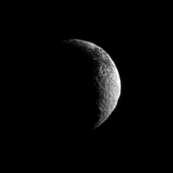 NASA Cassini spacecraft looks toward a crescent of Saturn dark and light moon, Iapetus.