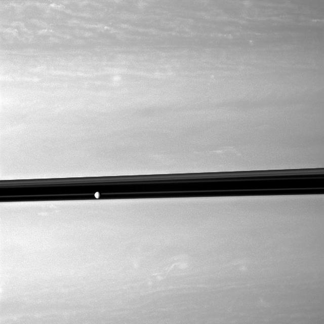 Saturn moon Enceladus orbits serenely before a backdrop of clouds roiling the atmosphere the planet in this image taken by NASA Cassini spacecraft. This view looks toward the northern, sunlit side of the rings from just above the ringplane.