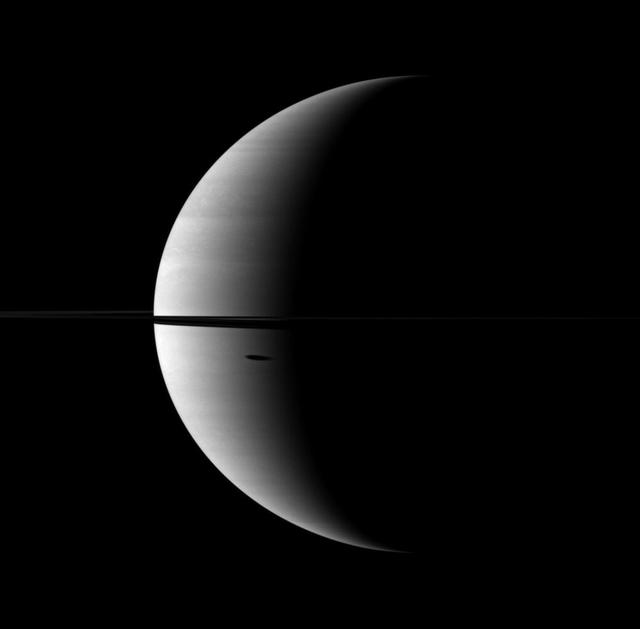 The shadow of Saturn moon Dione, cast onto the planet, is elongated in dramatic fashion in this image captured by NASA Cassini spacecraft. The moon itself does not appear here, but the shadow can be seen south of the ringplane.