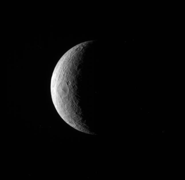 NASA Cassini spacecraft pictures a crescent of Saturn moon Rhea. Although craters dominate this particular view, the trailing hemisphere of Rhea also features wispy fractures.