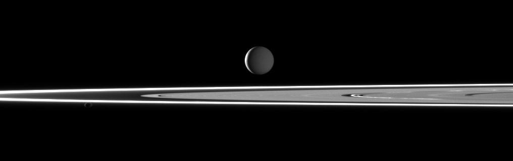 In this image taken by NASA Cassini spacecraft two light sources illuminate Saturn highly reflective moon Enceladus featuring bright rings and the small moon Pandora in the foreground.