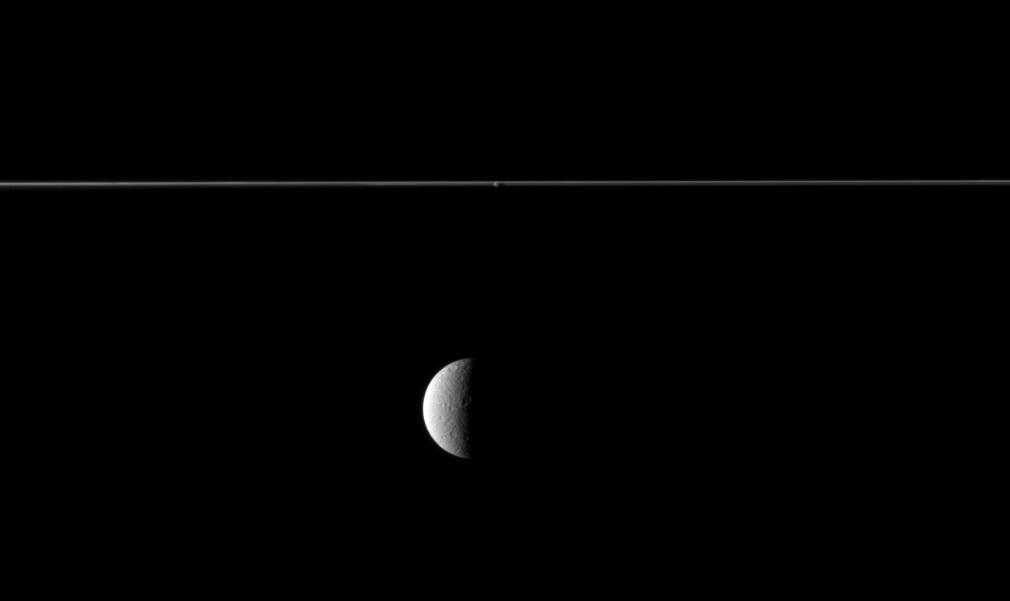 From just below the plane of Saturn rings, NASA Cassini spacecraft looks at the rings edge-on and sees the planet second largest moon beyond. Although Rhea may appear to be in the foreground of this image, it is not.