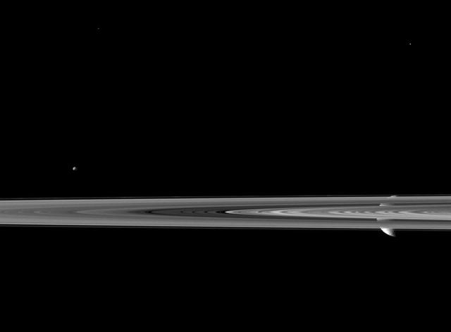 Saturn second largest moon Rhea pops in and out of view behind the planet rings in this image from NASA Cassini spacecraft, which includes the smaller moon Epimetheus.