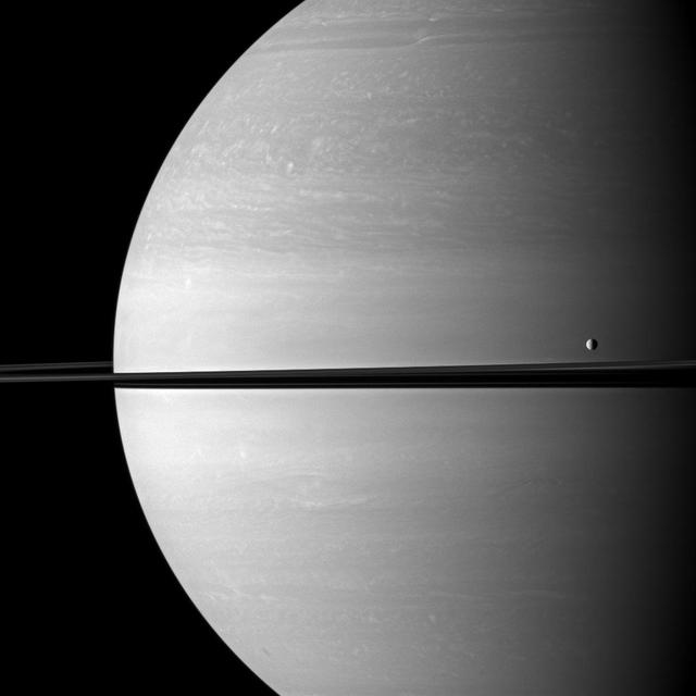 The moon Tethys occupies the right foreground of this Saturnian scene. This view from NASA Cassini spacecraft looks toward the anti-Saturn side of Tethys and toward the northern, sunlit side of the rings from just above the ringplane.