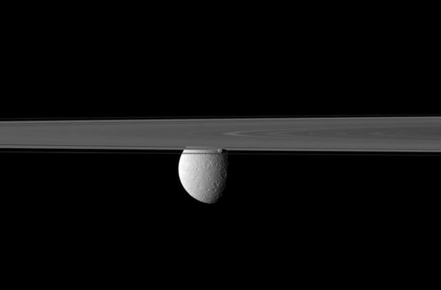 Saturn rings and small moon Prometheus obscure NASA Cassini spacecraft view of the planet second largest moon, Rhea. Prometheus can be seen just below the center of the image, in front of Rhea.