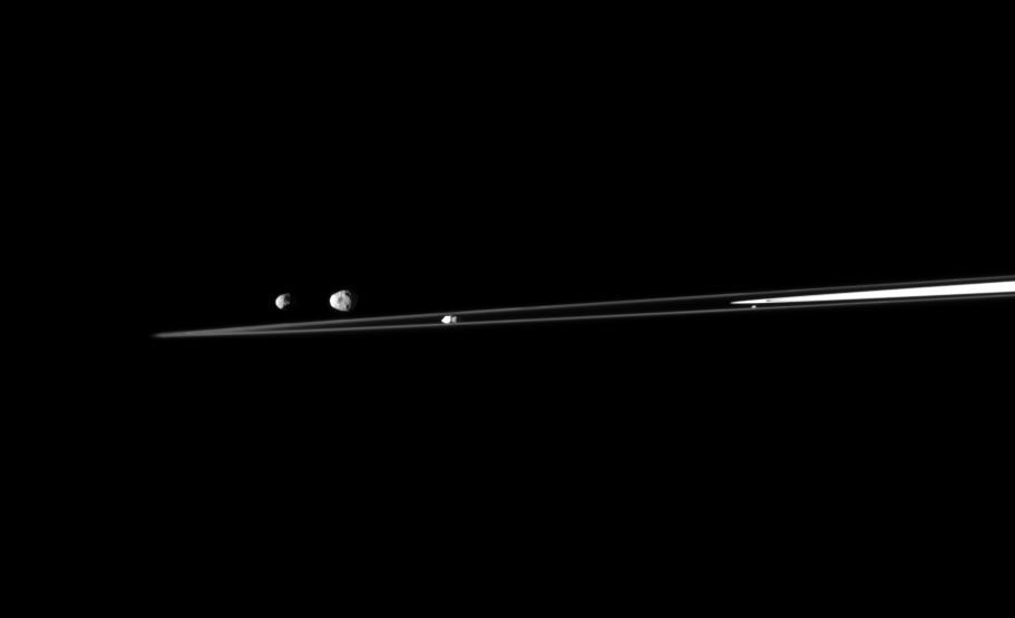 A quartet of Saturn moons are shown with a sliver of the rings in this view from NASA Cassini spacecraft. From left to right in this image are Epimetheus, Janus, Prometheus, and Atlas.