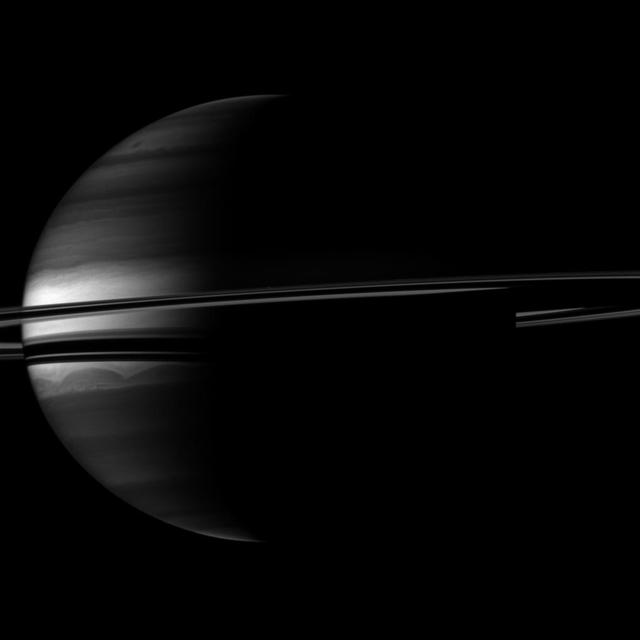 A crescent Saturn appears nestled within encircling rings in this image captured by NASA Cassini spacecraft. Clouds swirl through the atmosphere of the planet. Prometheus appears as a speck above the rings near the middle of the image.