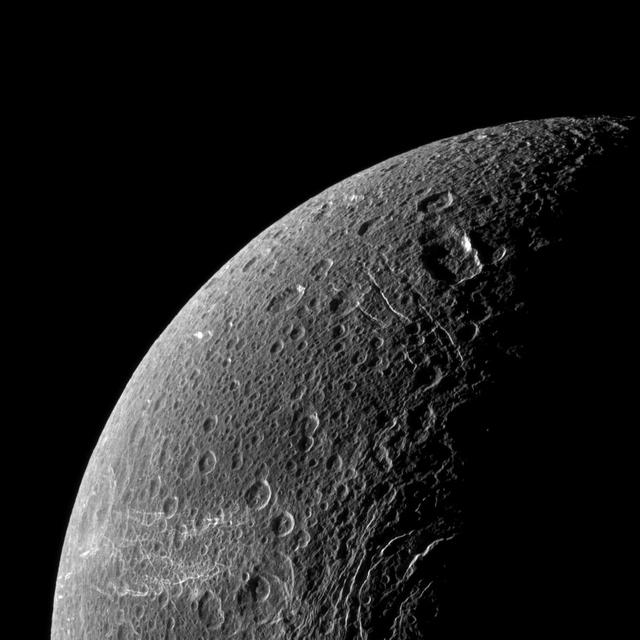Wispy terrain reflects sunlight brightly in the lower left of this NASA Cassini image of the northern latitudes of Saturn moon Dione.