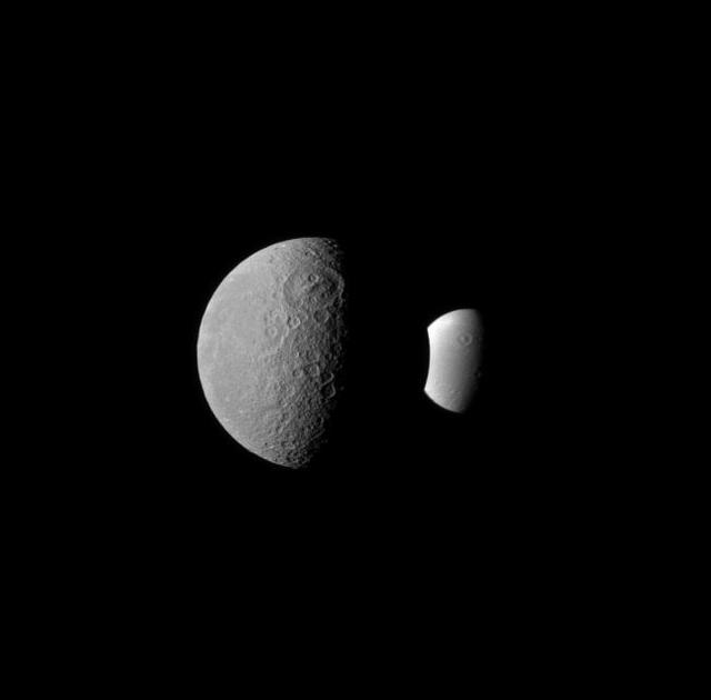 Rhea and Dione seem like dark and light fraternal twins in this image from NASA Cassini spacecraft, with each of these two Saturnian moons displaying a large crater oriented similarly in the northern hemisphere.