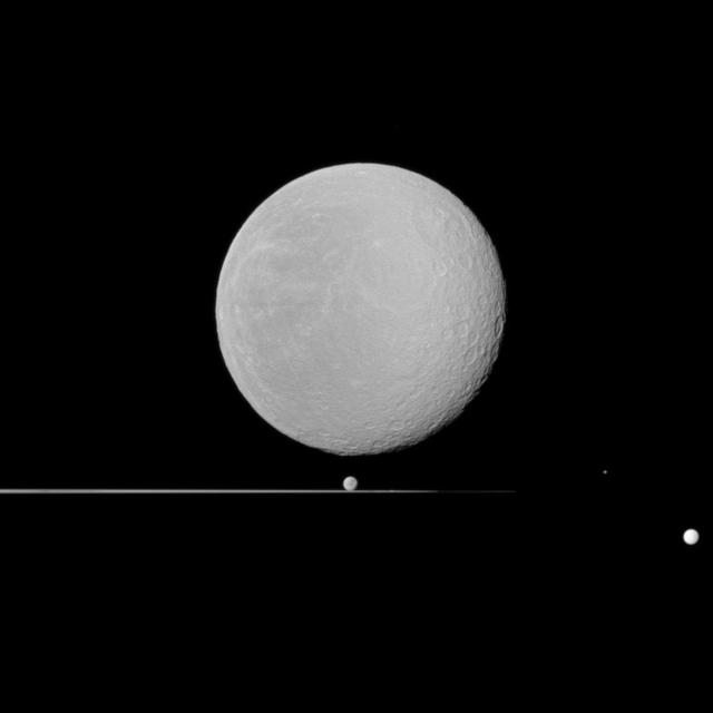 Five moons, dominated by Rhea in the foreground, share NASA Cassini spacecraft view with Saturn rings seen nearly edge-on. Also seen here are Dione, Epimetheus, Prometheus, and Tethys.