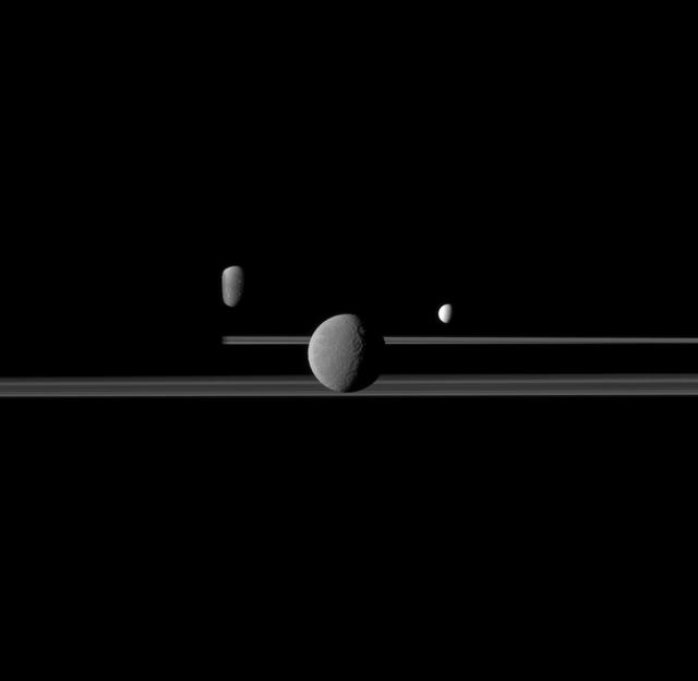 NASA Cassini spacecraft observes three of Saturn moons set against the darkened night side of the planet. Seen here are Rhea, closest to Cassini, Enceladus to right of Rhea, and Dione, left of Rhea.