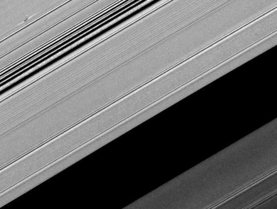A propeller-shaped structure created by an unseen moon appears dark in this image obtained by NASA Cassini spacecraft of the unilluminated side of Saturn rings. The propeller is marked with a red arrow in the top left.