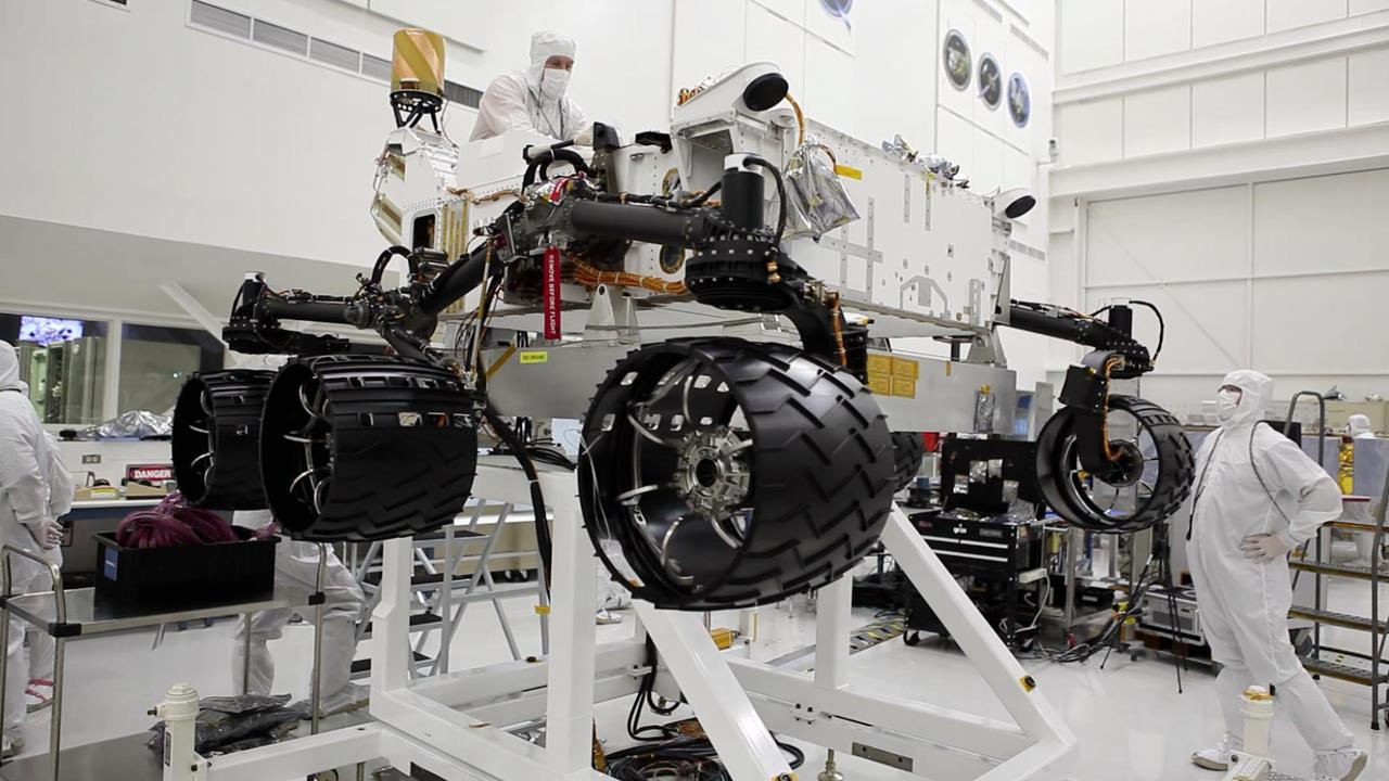 This image was taken in the cleanroom where NASA Curiosity rover is being assembled. It shows the rover, which is about the size of an SUV, hoisted on a white lift, with its black wheels suspended in the air.