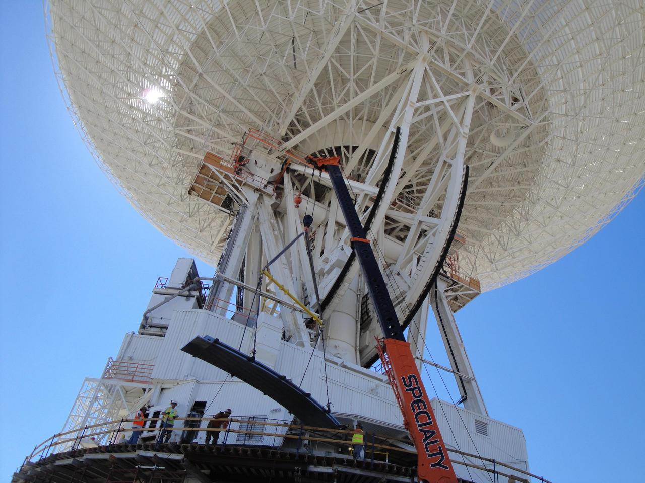 Under the unflinching summer sun, workers at NASA Deep Space Network complex in Goldstone, Calif., use a crane to lift a runner segment that is part of major surgery on a giant, 70-meter-wide antenna. 