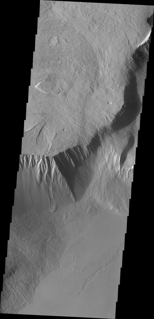 This image from NASA Mars Odyssey shows the southeast flank of Olympus Mons. This huge volcano is surrounded by an escarpment, a large cliff at the volcano margin; a landslide lies alongside the escarpment.