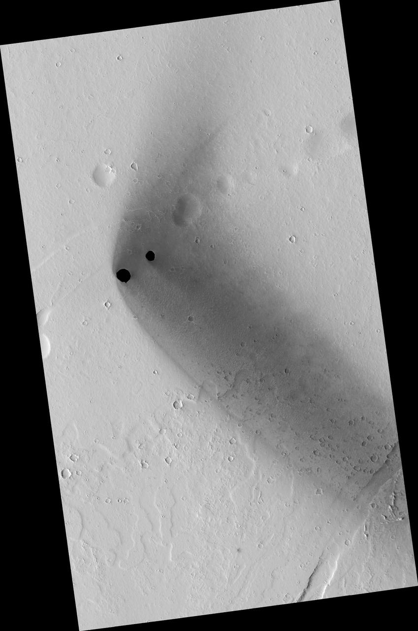 Two dark, rimless pits are located to the northwest of Ascraeus Mons in the Tharsis volcanic region of Mars in this image from NASA Mars Reconnaissance Orbiter. They are situated in the midst of a wispy, dark, boomerang-shaped deposit.