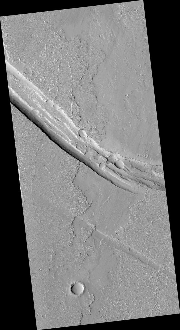 This image from NASA Mars Reconnaissance Orbiter shows a graben a trough formed when the ground drops between two parallel faults and a lava flow in the Tharsis volcanic province of Mars. North is up.