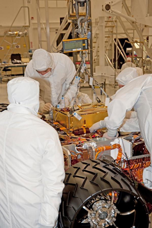 In this photograph, technicians and engineers inside a clean room at NASA Jet Propulsion Laboratory, Pasadena, Calif., position NASA Sample Analysis at Mars SAM above the mission Mars rover, Curiosity, for installing the instrument.