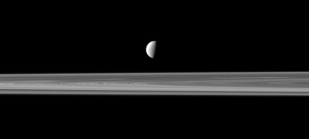 Saturn fourth largest moon, Dione, appears like a solitary ornament suspended above the rings in view from NASA Cassini spacecraft. The rings are closer to Cassini in this view, with Dione more distant.