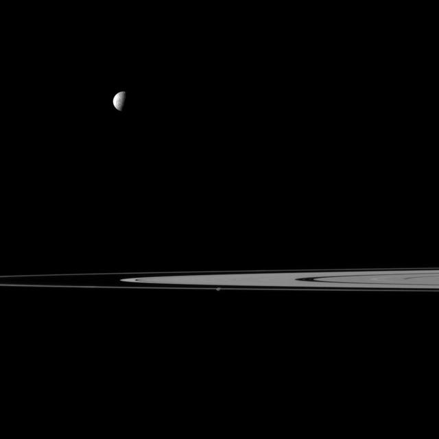 Saturn rings lie between a pair of moons in this view from NASA Cassini spacecraft that features Mimas and Prometheus. Mimas is the more noticeable of the two moons at top left, Prometheus is near the center of image and closest to Cassini.