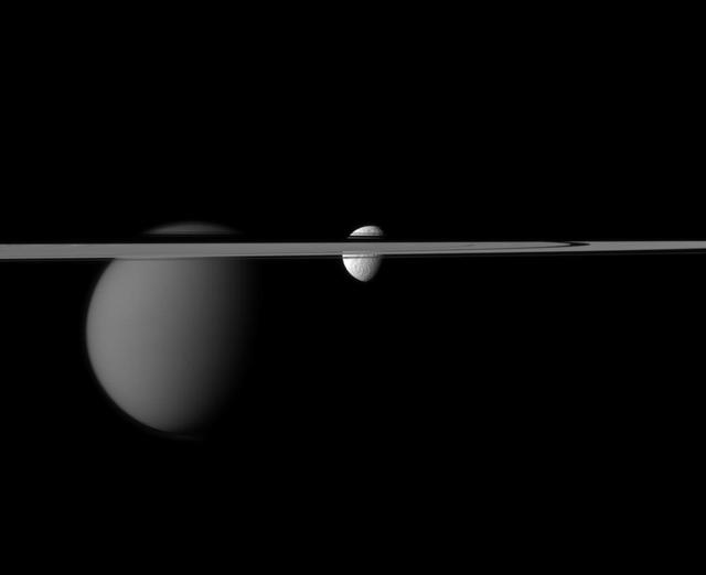 The line of Saturn rings disrupts NASA Cassini spacecraft view of the moons Tethys and Titan. Larger Titan is on the left. Tethys is near the center of the image.