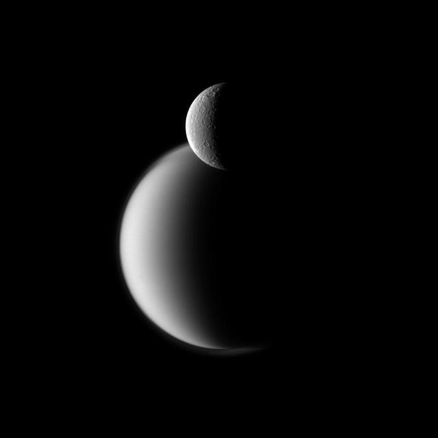 Craters appear well defined on icy Rhea in front of the hazy orb of the much larger moon Titan in this view from NASA Cassini spacecraft.
