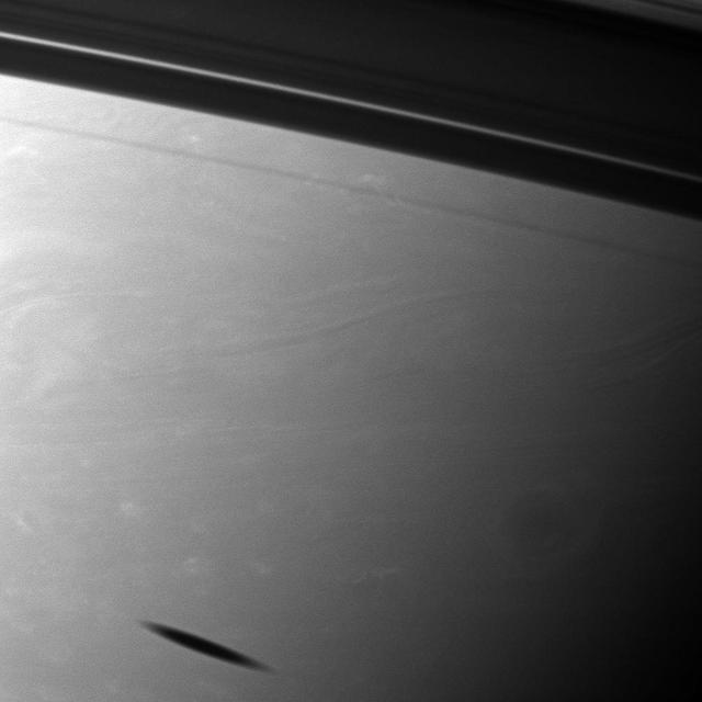 The shadow of the moon Mimas creates a smudge on the southern hemisphere of Saturn in this view from NASA Cassini spacecraft. Mimas does not appear here, but it does cast its shadow on the planet in the lower left of the image.