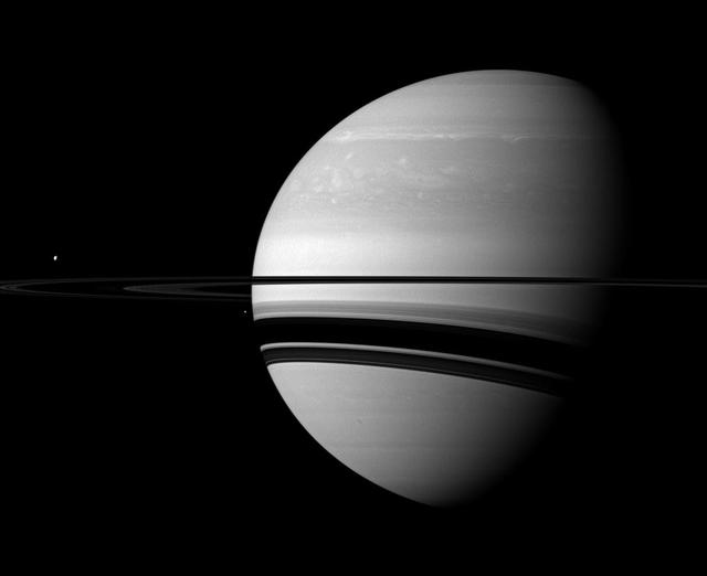 A pair of Saturn many moons joins the planet in this scene captured by NASA Cassini spacecraft. Tethys appears as a small white dot above the rings on the far left, Enceladus appears as a smaller bright speck beside the planet.