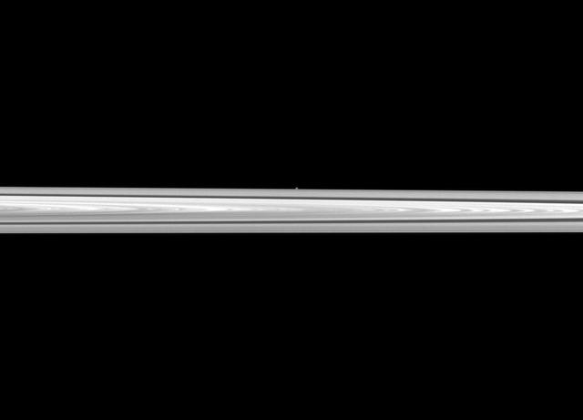 NASA Cassini spacecraft looks past Saturn main rings to spy the tiny moon Atlas, which orbits between the main rings and the thin F ring. The main rings are closer to the spacecraft than Atlas is, and the moon appears as only a small, white dot.