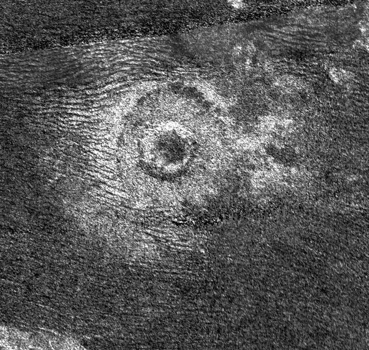 Impact craters are rare on Titan. Until recently only seven had been identified definitely on Titan. Dunes, visible as dark lines on the left of the image, have been swept toward the crater by the winds of Titan.