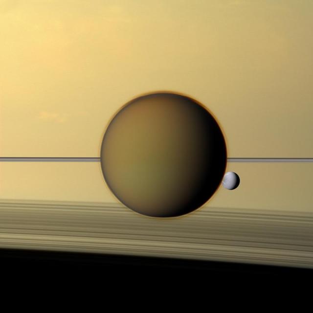 Saturn fourth-largest moon, Dione, can be seen through the haze of the planet largest moon, Titan, in this view of the two posing before the planet and its rings from NASA Cassini spacecraft.
