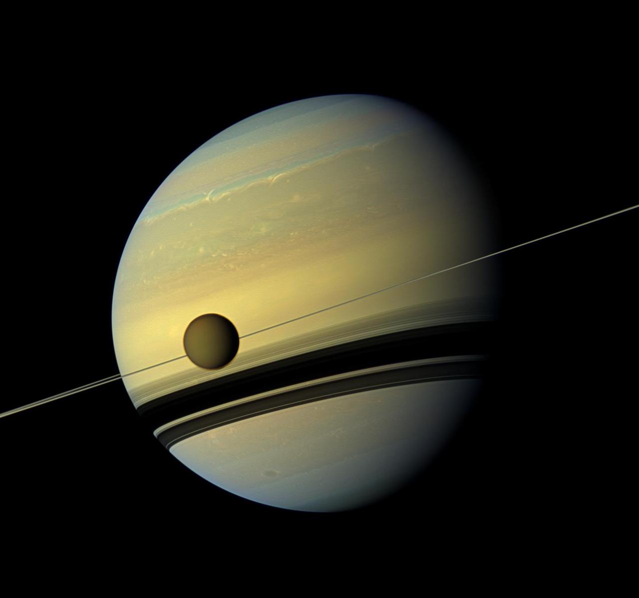 A giant of a moon appears before a giant of a planet undergoing seasonal changes in this natural color view of Titan and Saturn from NASA Cassini spacecraft.
