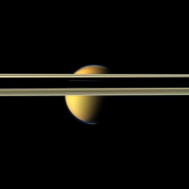 Saturn rings obscure part of Titan colorful visage in this image from NASA Cassini spacecraft. The south polar vortex that first appeared in Titan atmosphere in 2012 is visible at the bottom of this view.