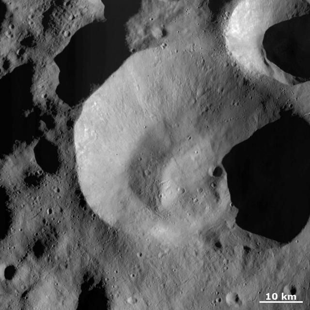 This image from NASA Dawn spacecraft is dominated by Caparronia impact crater, approximately 55 km in diameter with a mostly fresh, irregularly shaped rim. It also has a curved, linear mound running across most of its base.